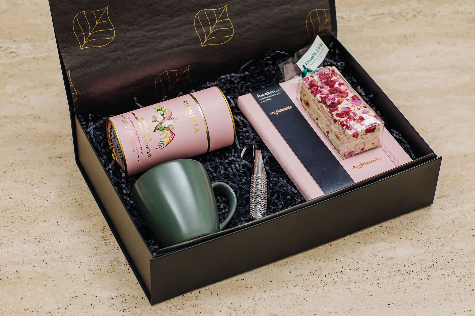 A curated gift hamper with tea, a ceramic mug, a journal and sweet treats